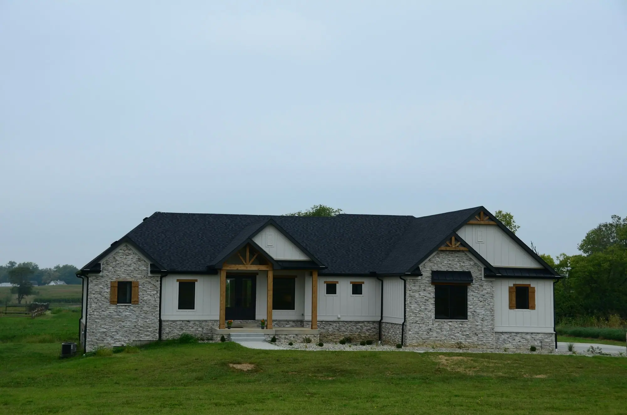 Stone bungalow with black roof and large windows on a rural lot