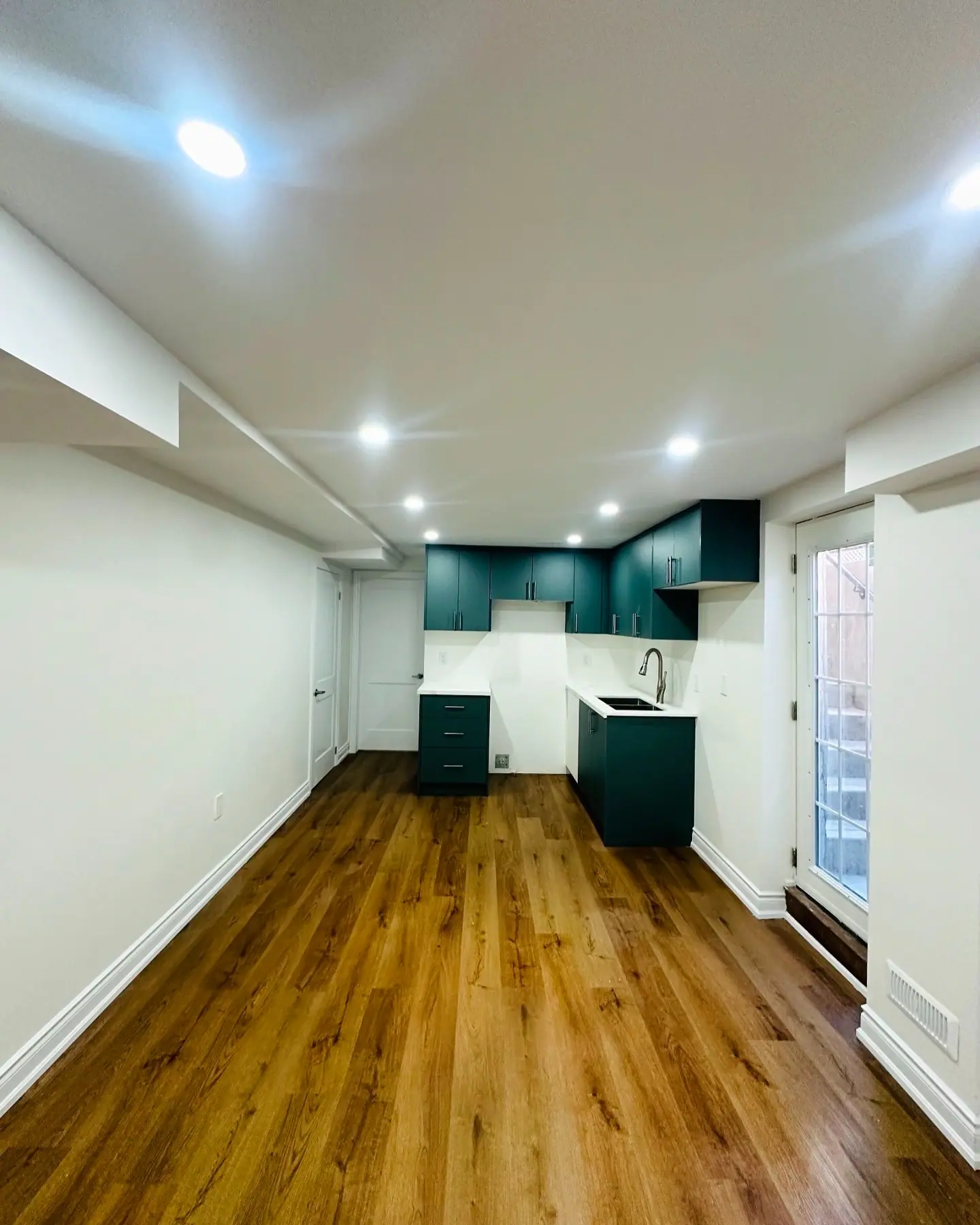 Basement with walnut-tone vinyl plank flooring and teal kitchen cabinets