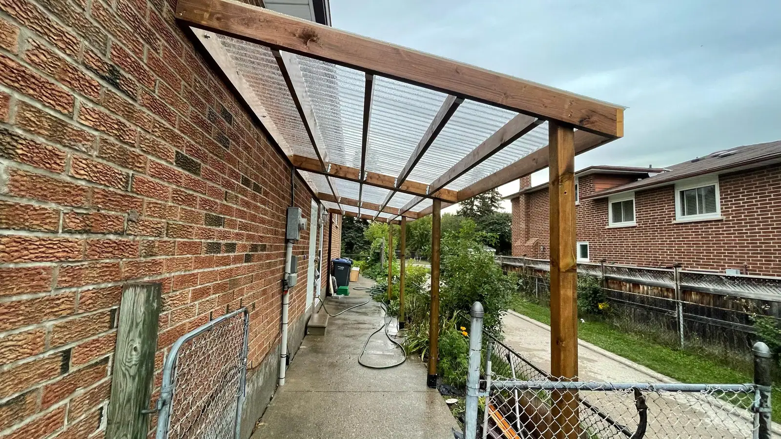Attached pergola with a clear roof along a brick house