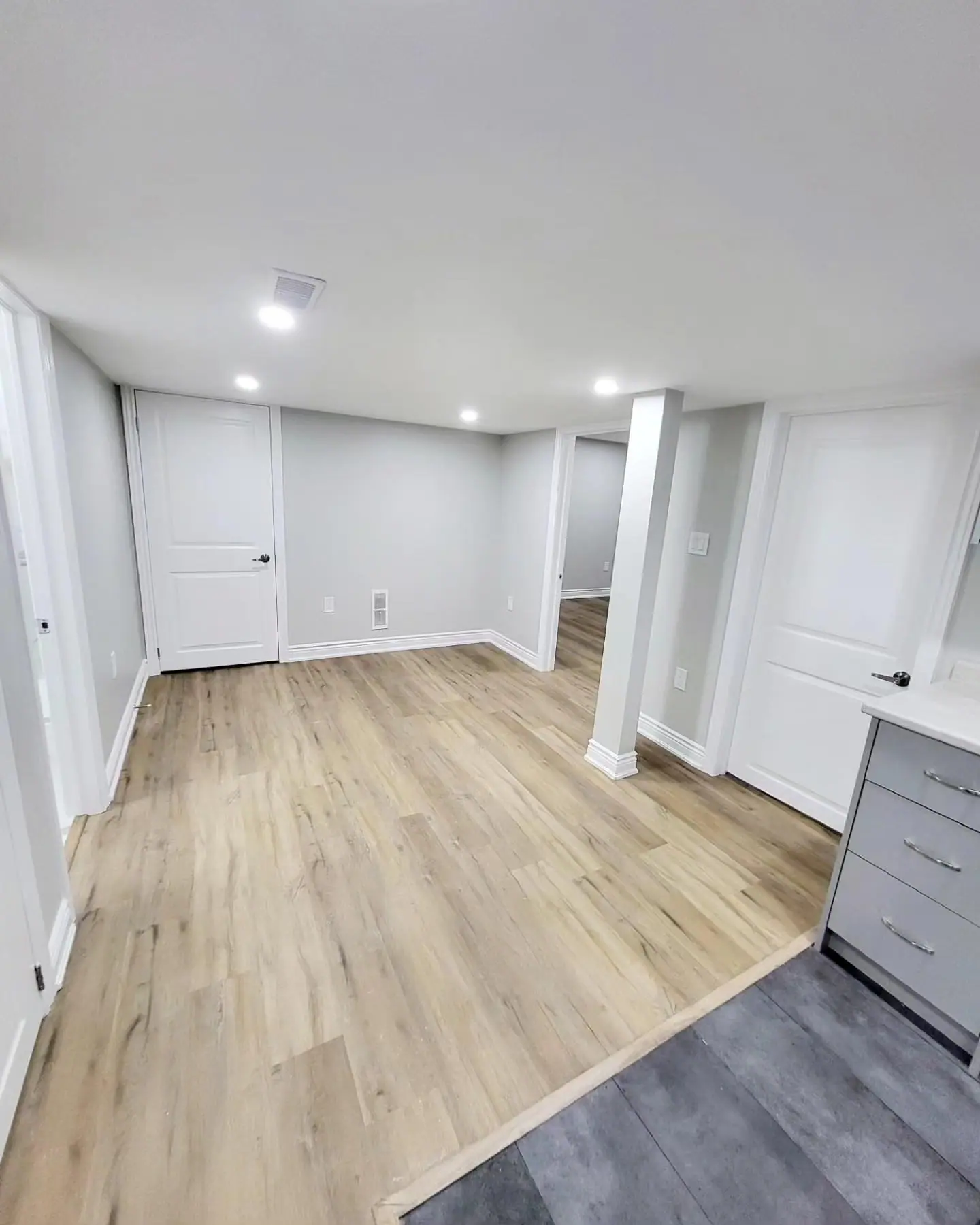 Bright finished basement room with light vinyl plank flooring and pot lights