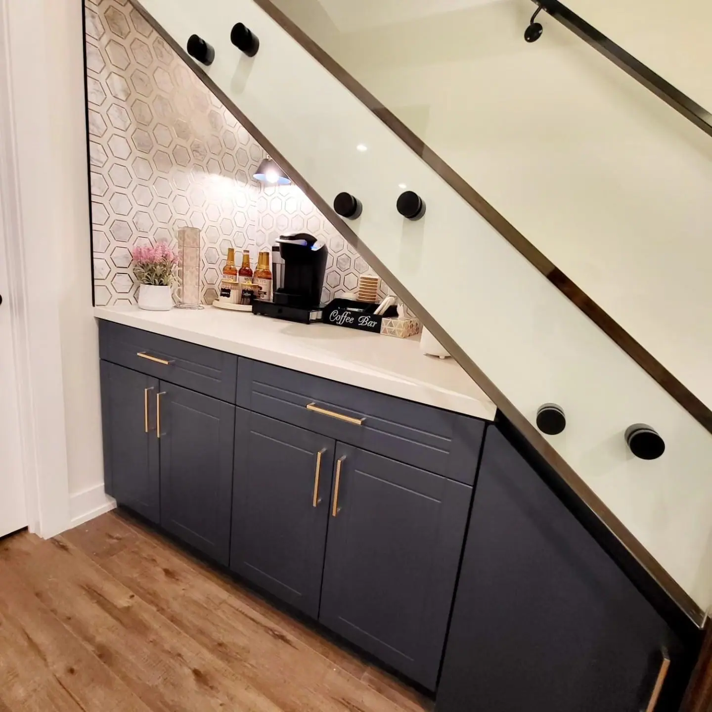 Under-stair basement coffee bar with navy cabinets and glass stair railing
