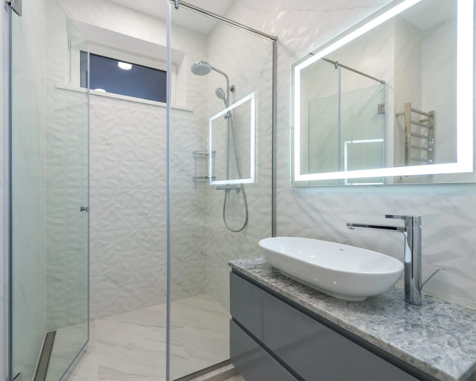 Vessel sink vanity with LED mirror beside a glass shower