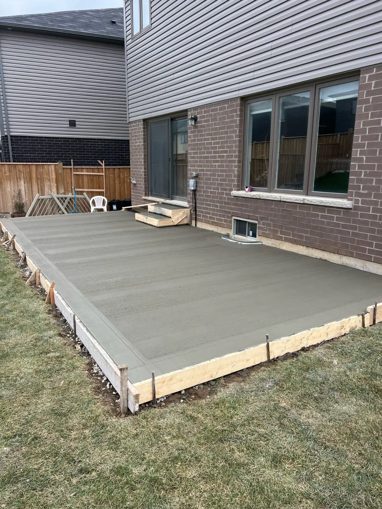 Freshly poured concrete patio pad behind a brick house